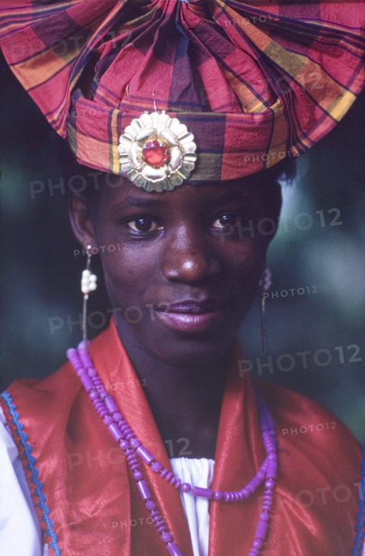 Dancer at the Caribbean Music Village. Head and shoulders portrait of a female dancer at the Caribbean Music Village, a cultural festival held at the Commonwealth Institute. She wears traditional Caribbean costume and jewellery including a fanned headdress decorated with a pin brooch. London, England, 7-26 July 1986. London, London, City of, England (United Kingdom), Western Europe, Europe .