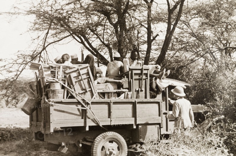 Jeep made ready for safari. African porters sit amongst a jumble of folding tables and chairs in the back of a jeep, waiting to leave on safari. Kenya, circa 1935. Kenya, Eastern Africa, Africa.