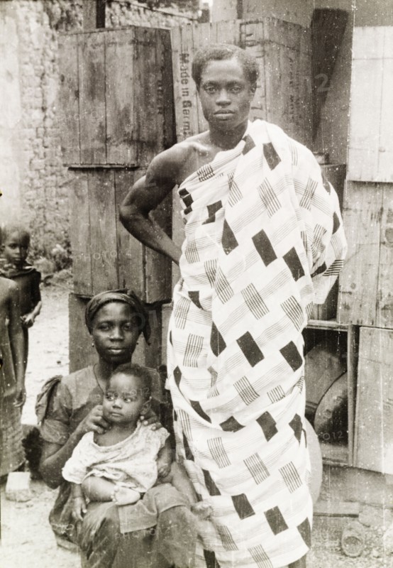An Asante family. An Asante (Ashanti) man stands beside his seated wife and baby, wearing a traditional patterned robe. Asante, Gold Coast (Ghana), circa 1950., Ashanti, Ghana, Western Africa, Africa.