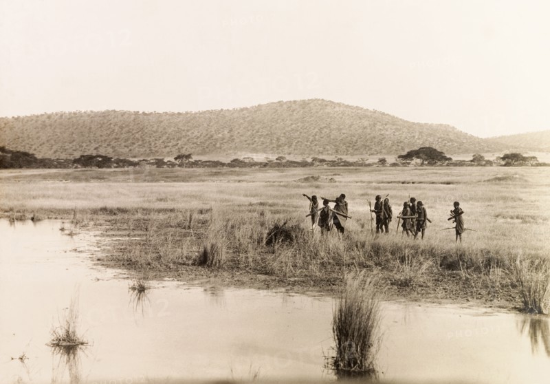 Okiek hunters at Lake Ol Bolossat. A group of Okiek hunters, armed with bows and arrows, search for prey on the shores of Lake Ol Bolossat. Central Kenya, circa 1900., Central (Kenya), Kenya, Eastern Africa, Africa.