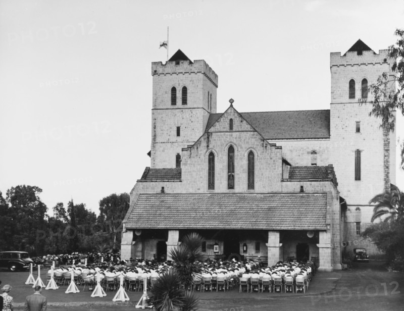Memorial service for King George VI, Nairobi. A congregation of mourners sit on chairs with their heads bowed outside All Saints Cathedral during a memorial service for King George VI, who died in his sleep at Sandringham House, England, on 6 February 1952. Nairobi, Kenya, circa 6 February 1952. Nairobi, Nairobi Area, Kenya, Eastern Africa, Africa.