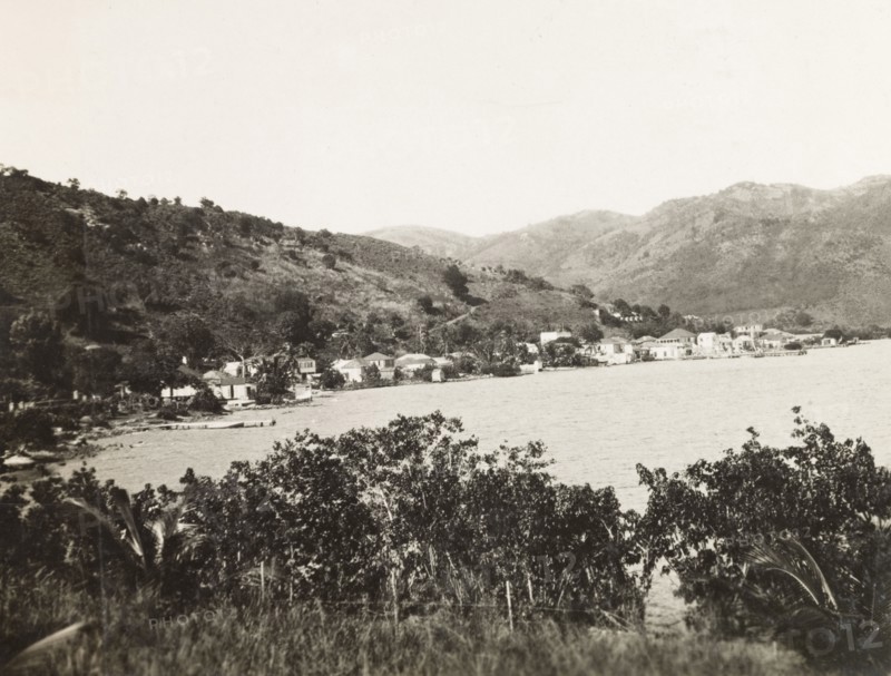 Coastline of Tortola. View along a stretch of coastline on the island of Tortola, where a small settlement borders the Caribbean Sea at the foot of a mountainous slope. Tortola, British Virgin Islands, circa 1931., Tortola, British Virgin Islands, Caribbean, North America .