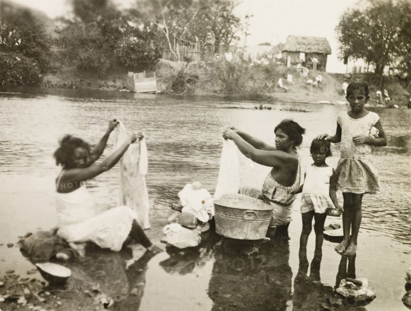 Washing clothes in a stream. Two female plantation workers, accompanied by two young girls, sit in a shallow stream washing their clothes. Trinidad and Tobago, circa 1931., Trinidad and Tobago, Trinidad and Tobago, Caribbean, North America .
