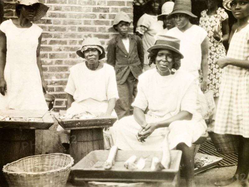 Fish stall in St Lucia. A female trader sits smoking a pipe at her street stall, where she sells fish displayed on a tray. St Lucia, circa 1931., St Lucia, St Lucia, Caribbean, North America .