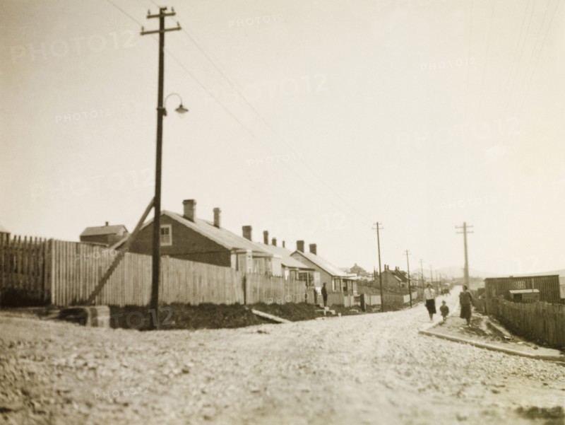 Stanley, East Falkland. View down a gravel road stretching past a row of colonial-style houses and into the distance. Stanley, Falkland Islands, circa 1931. Stanley, East Falkland, Falkland Islands, South Atlantic Ocean, South America .