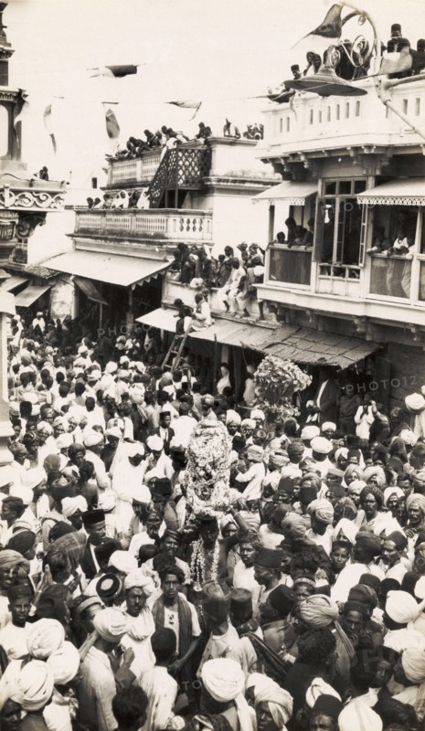 Street festival in Secunderabad. Crowds of people carry religious icons decorated with garlands as they process through a city street during a festival, possibly the Hindu Ganesh Festival (Ganesh Chaturthi). Spectators watch the festivities from nearby rooftops and balconies. Secunderabad (Hyderabad), Andhra Pradesh, India, circa 1930. Hyderabad, Andhra Pradesh, India, Southern Asia, Asia.
