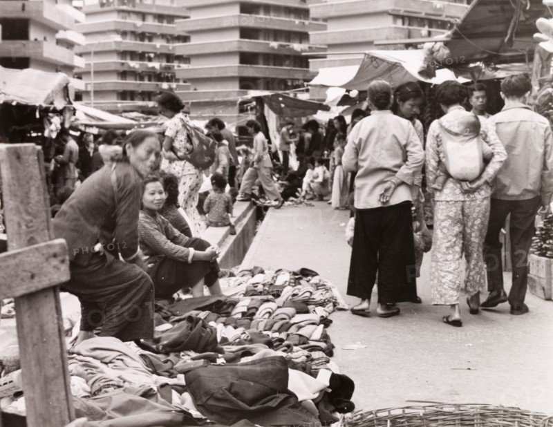 Clothes market in Hong Kong. Street traders display their wares at a busy clothes market. Behind them are several multi-storey resettlement blocks, which were built all over Kowloon by the British government to re-house 70,000 people after fire destroyed an overcrowded squatter settlement in 1953. Kowloon, Hong Kong, China, 1963. Kowloon, Hong Kong, China, People's Republic of, Eastern Asia, Asia.