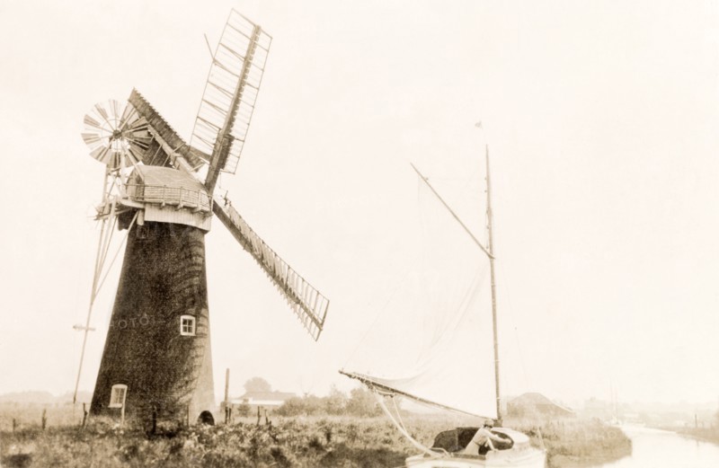 Sailing on the Norfolk Broads. A boat sails past a windmill as it travels along a river on the Norfolk Broads. Norfolk, England, 1930., Norfolk, England (United Kingdom), Western Europe, Europe .