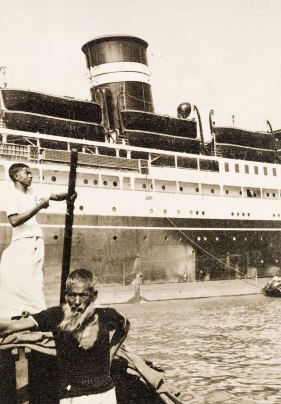 Ferry across the Hooghly River. A 'sarang' (senior crew member) ferries people across the Hooghly River on a dinghy to board a large steamship moored at Calcutta docks. Calcutta (Kolkata), India, circa 1931. Kolkata, West Bengal, India, Southern Asia, Asia.