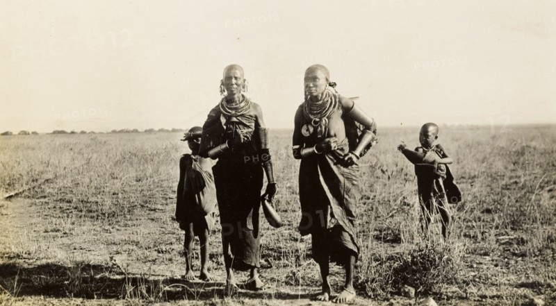 Maasai women and children collecting wood. Two Maasai women and two young children carry bundles of firewood and gourds of water in the Sanya Plains. Kilimanjaro, Tanganyika Territory (Tanzania), circa 1930., Kilimanjaro, Tanzania, Eastern Africa, Africa.