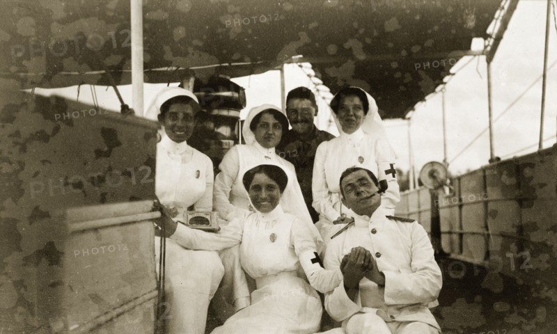 British officers with Indian nurses. Two British military officers pose on the deck of a ship with four Indian nurses. One of the men appears to be wearing a white naval uniform, whilst the other seems to be dressed in khaki army attire. Related images suggest the group were involved with the British offensive against German East Africa (Tanzania) during the First World War (1914-18). Probably Indian Ocean, circa 1914., Indian Ocean, Africa.