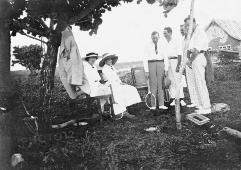 Tennis party at Kitimura Estate. Six European friends gather for a game of tennis at Kitimura Estate, the home of settler farmers Jos (standing with racquet) and Nellie Grant (left, seated). The Grants arrived in Kenya in 1912 to set up a coffee farm and were joined in 1914 by their seven year old daughter, Elspeth (later Huxley). Thika, Kenya, 1914. Thika, Nairobi Area, Kenya, Eastern Africa, Africa.