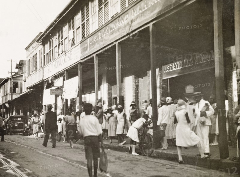 Frederick Street, Port of Spain. Crowds bustle about on Frederick Street outside a row of commercial buildings. Port of Spain, Trinidad, circa 1931. Port of Spain, Trinidad and Tobago, Trinidad and Tobago, Caribbean, North America .