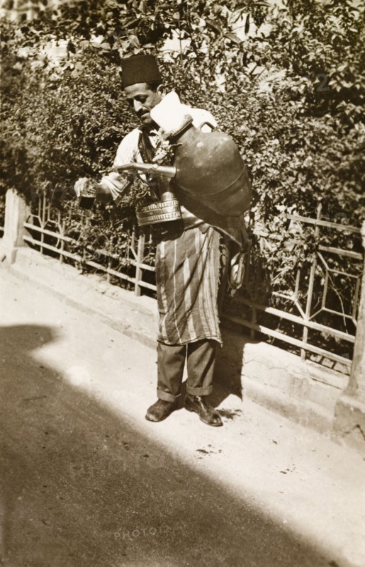 Lemonade seller, Palestine. A lemonade seller pours out a drink from a large jug strapped to his side, as he stands on a roadside plying for trade. British Mandate of Palestine (Middle East), circa 1942., Middle East, Asia.