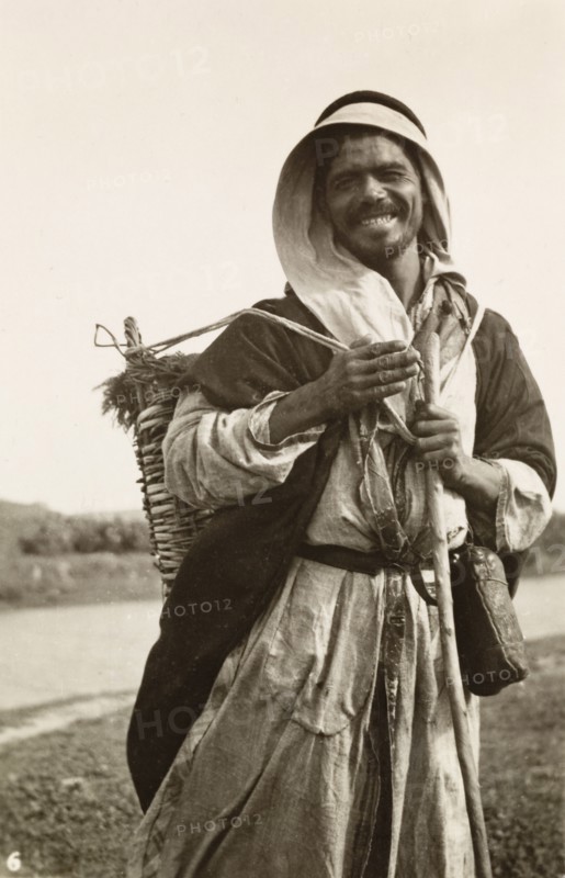 Portrait of a Palestinian bedouin man. Portrait of a smiling bedouin man, who carries a large basket strapped on his back as he travels along a rural road. British Mandate of Palestine (Middle East), circa 1942., Middle East, Asia.