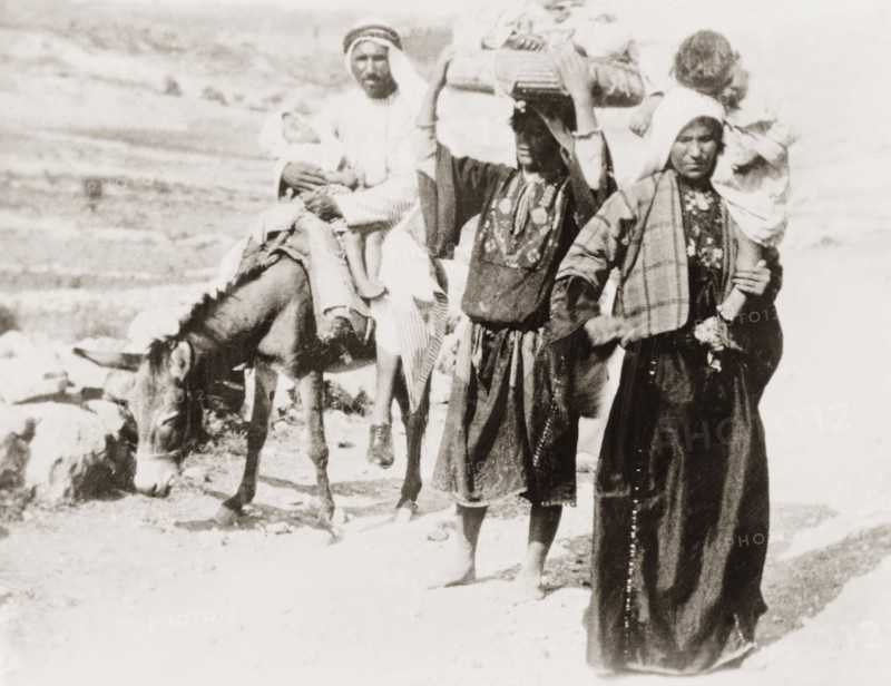 Arab family on a rural road. An Arab family travel along a rural road with two sleeping children. The women walk, and both wear traditional embroidered 'thobs'. British Mandate of Palestine (Middle East), circa 1938., Middle East, Asia.