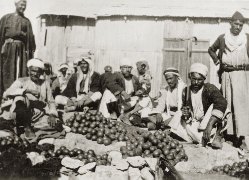 Oranges for sale, Palestine. Several Arab men sit on the ground, surrounded by heaps of oranges for sale at an outdoor market. British Mandate of Palestine (Middle East), circa 1938., Middle East, Asia.