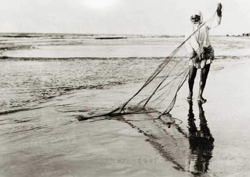 A Palestinian fisherman. An elderly Arab fisherman detangles his fishing net in shallow surf on a sandy beach. British Mandate of Palestine (Middle East), circa 1938., Middle East, Asia.