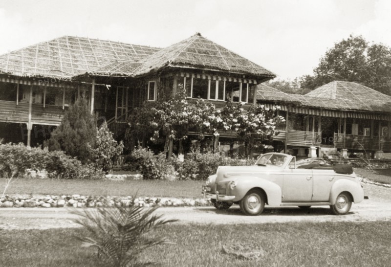 A stilted bungalow in British Malaya. A small car is parked in the driveway outside Dr Tweedie's house, a stilted bungalow with a thatched roof made from palm leaves. Sungei Siput near Ipoh, British Malaya (Malaysia), August 1940. Ipoh, Perak, Malaysia, South East Asia, Asia.