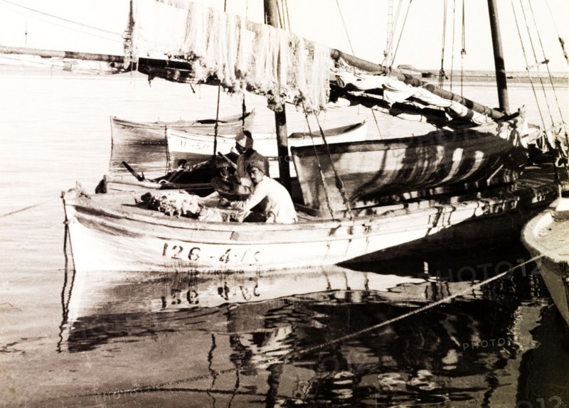 Fishing boat on the Suez Canal. Two fishermen sit aboard a stationary sail boat on the Suez Canal, beneath a row of fishing nets hung up over the boom. Suez, Egypt, circa 1930. Suez, Suez, Egypt, Northern Africa, Africa.