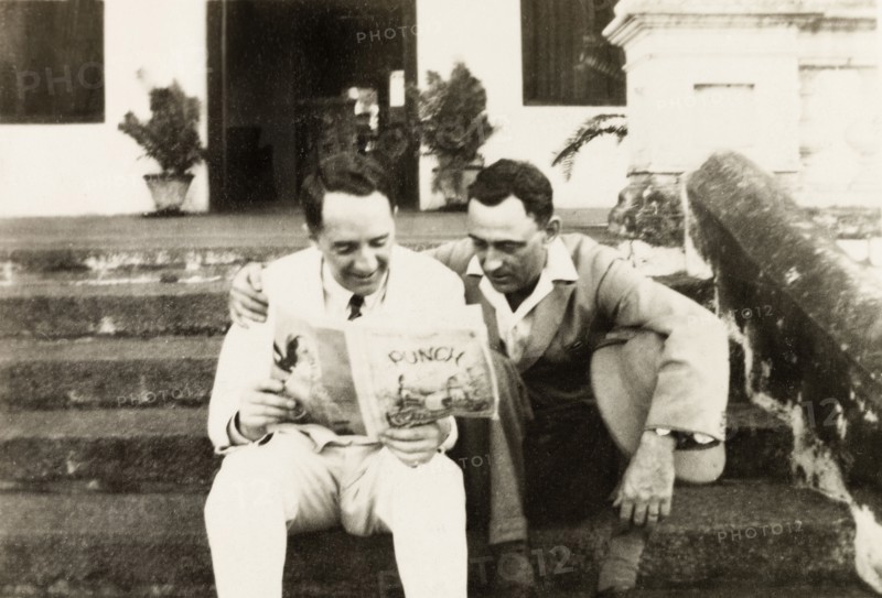 Reading 'Punch' magazine. Mr Moulton and Mr Horler sit on the steps of the United Theological College reading a copy of Punch magazine. Bangalore, India, circa 1932. Bangalore, Karnataka, India, Southern Asia, Asia.