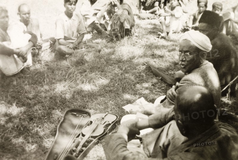 Evangelist preaching to plantation workers. A Methodist evangelist called D. Anniah sits in a circle with a group of plantation workers, his violin positioned in an open case beside him. D. Anniah was accompanying British missionary Reverend Norman Sargant, who travelled throughout Mysore State preaching to rural Christian communities. Mysore State (Karnataka), India, 1934., Karnataka, India, Southern Asia, Asia.