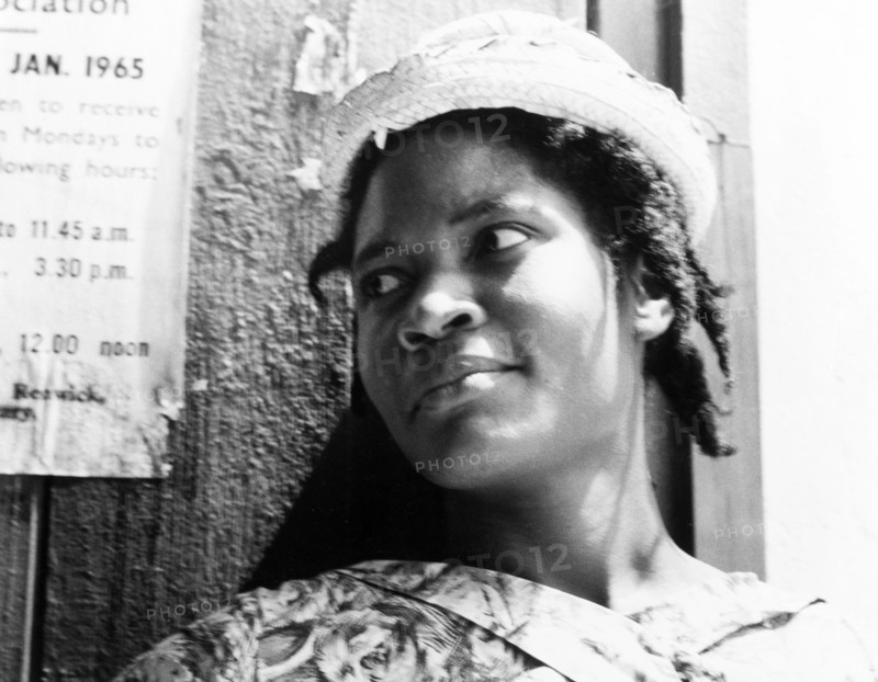 Portrait of a Grenadian woman. Portrait of a young Grenadian woman, dressed smartly in a patterned dress and woven hat with her hair in braids. Grenada, 1965. Grenada, Caribbean, North America .