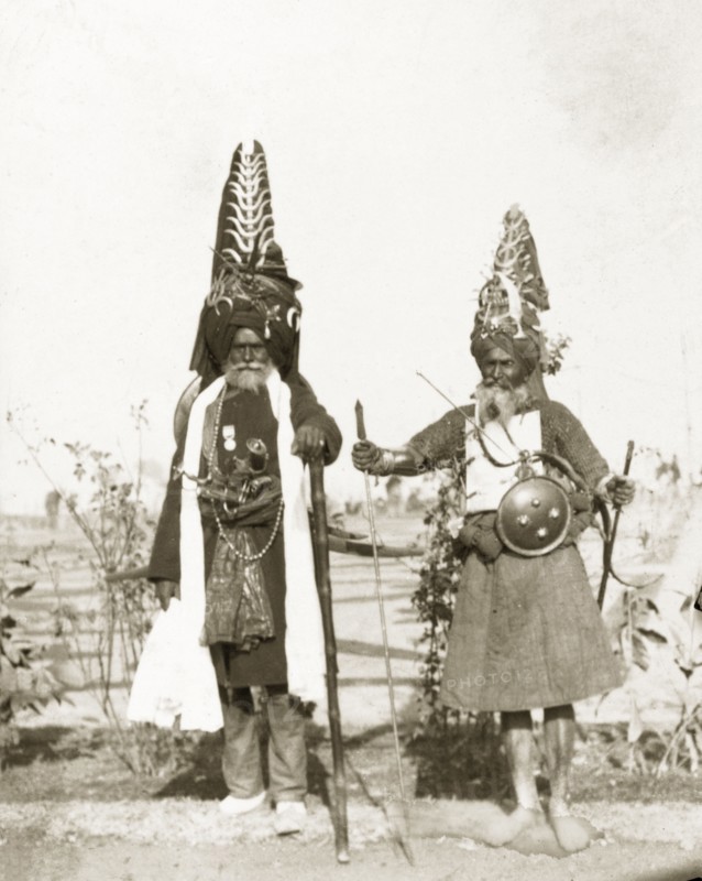 Akalis at Coronation Durbar, 1903. Full-length portrait of two Akalis (Nihang), prestigious Sikh warriors, who wear traditional, tall turbans coiled with steel, in which to store weapons such as knives, swords, and kirpans (Sikh ceremonial daggers). These Akalis had travelled from the Harimandir Sahib (Golden Temple) in Amritsar, Punjab, to Delhi to attend Edward VII's Coronation Durbar. Delhi, India, circa 1 January 1903. Delhi, Delhi, India, Southern Asia, Asia.