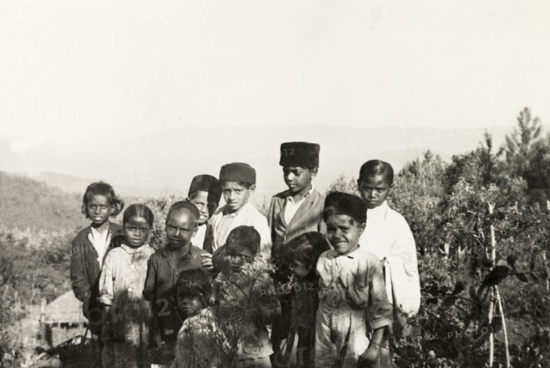 Students of a mission school, Mysore State. Students of Pandaravalli School pose for an infomal portrait by a thicket of cultivated coffee plants. The school was founded by Methodist missionaries to educate the children of plantation workers at Pandaravalli coffee estate. Mysore State (Karnataka), India, circa 1937., Karnataka, India, Southern Asia, Asia.