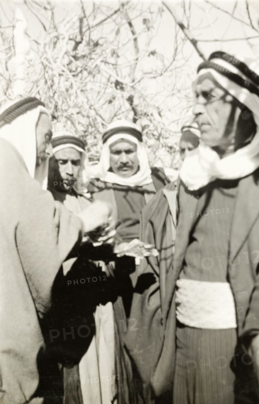 Arab villagers exchange money. Arab villagers wearing 'keffiyehs' (headdresses) exchange money during a meeting with William Ryder McGeagh, District Commissioner in Jerusalem. British Mandate of Palestine (Israel), circa 1940. Israel, Middle East, Asia.