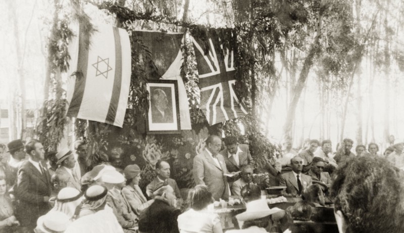Opening of the Benes Garden in Gan Yavne. A man identified as 'Novak' addresses a seated audience at the opening of the Benes Garden in commemoration of deposed Czech President, Edvard Benes. Behind him hangs a framed portrait of Benes, surrounded by a Jewish flag and a union jack. Gan Yavne, British Mandate of Palestine (Central Israel), 4 June 1944., Central (Israel), Israel, Middle East, Asia.