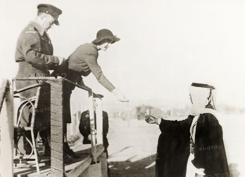 At a camel race in Be'er Sheva. The wife of William Ryder McGeagh, District Commissioner in Jerusalem, accepts a token from an Arab man during a camel race at Be'er Sheva. The man in uniform to her right is identified as 'Cullingham'. Be'er Sheva, British Mandate of Palestine (South Israel), 27 February 1944. Be'er Sheva, South (Israel), Israel, Middle East, Asia.