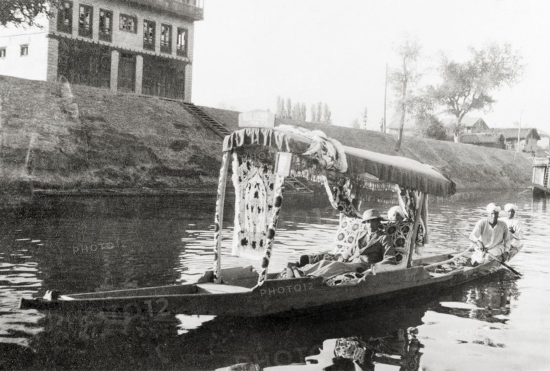 Water taxi on a Srinagar canal. Majid Ullah in the shikari 'Blue Heaven' as he is ferried along a canal in a water taxi. Srinagar, Jammu and Kashmir, India, May 1934. Srinagar, Jammu and Kashmir, India, Southern Asia, Asia.