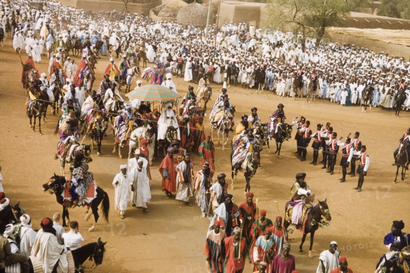 The Emir of Kano rides into the Residency. The new Emir of Kano, Alhaji Ado Bayero, rides into the Residency beneath a ceremonial umbrella during a colourful procession for Sallah, an Islamic celebration held to mark the end of Ramadan. Kano, Nigeria, 1963. Kano, Kano, Nigeria, Western Africa, Africa.