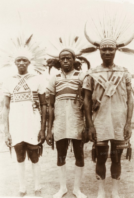Three Zulu rickshaw pullers. Portrait of three Zulu rickshaw pullers. They wear distinctive headgear made from animal horns and feathers, and are decorated with white body paint on their feet and lower legs. Durban, Natal (KwaZulu-Natal), South Africa, 1918. Durban, KwaZulu Natal, South Africa, Southern Africa, Africa.