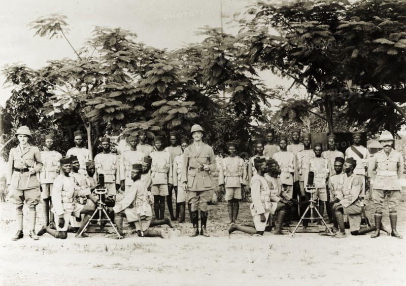Artillery company of the Nigeria Regiment. Three British officers pose with an artillery company of the Nigeria Regiment of the Royal West African Frontier Force. Several African soldiers kneel around two machine guns on tripods at the front of the group. Nigeria, circa 1918. Nigeria, Western Africa, Africa.