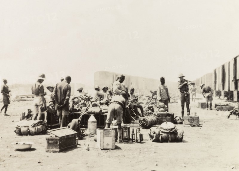 Schutztruppes unload supplies from a train. German and African schutztruppes organise their luggage and army supplies after arriving by freight train at a military post. German East Africa (Tanzania), circa 1910. Tanzania, Eastern Africa, Africa.