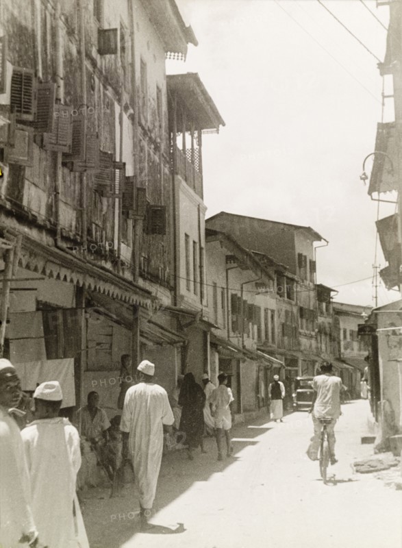 Commercial street in Stone Town. Tall, narrow shops with shuttered windows and awnings flank a commercial street in Stone Town. Stone Town, Zanzibar (Tanzania), 1947. Stone Town, Zanzibar Urban/West, Tanzania, Eastern Africa, Africa.