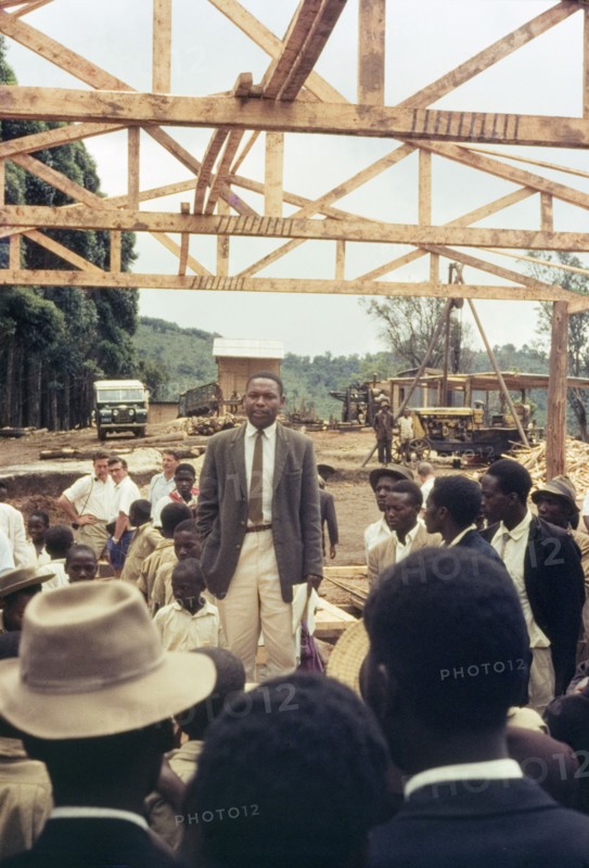 Mr Bitware speaks at Mafuga sawmill. Mr J. Bitwari addresses a crowd of Ugandan chiefs, villagers and schoolchildren during a forestry open day at Mafuga sawmill. Above him is a partly finished mill building comprising upright beams and roof trusses. Mafuga, Kigezi, South West Uganda, September 1963., West (Uganda), Uganda, Eastern Africa, Africa.