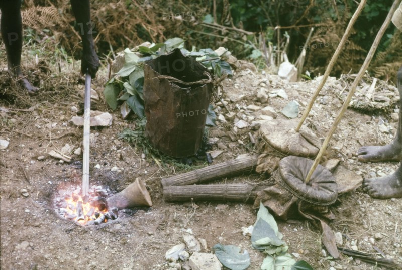 Iron Age forge in Mafuga Forest. A forge used by forestry workers to harden the tips of rock drills whilst clearing a track to Mafuga Forest nursery. A related caption explains: "A charcoal fire... was fanned by two... clay pipes and bellows made of a goat-skin... The white hot tips of the drills were hammered to a chisel edge, reheated and tempered in a battered debbi of water". Kigezi, South West Uganda, September 1963., West (Uganda), Uganda, Eastern Africa, Africa.
