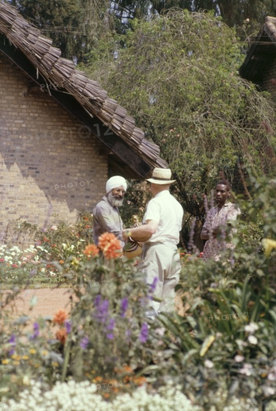 Making friends at the White Horse Inn. Alan, the father of District Forest Officer James Lang Brown, befriends an elderly Sikh man at the White Horse Inn in Kabale. A related caption comments: "The Sikhs filled a niche in East Africa, being expert craftsmen - carpenters, engineers and of course sawmillers and ginners. All of them charming, and some of them rogues". Kabale, West Uganda, July 1962. Kabale, West (Uganda), Uganda, Eastern Africa, Africa.