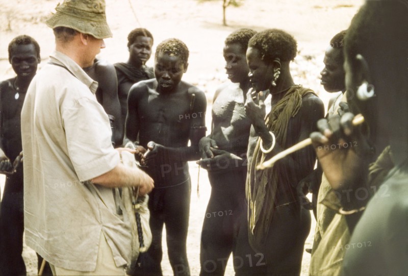 Tobacco exchanged for news. British Game Ranger John Blower offers tobacco to a group of Toposa men at Kabekanyang on the Uganda-Sudan border. In return, he receives the 'habari' (news) about "game movements, poachers, marauders, cattle rustlers". Kabekanyang, North East, Uganda, 1959., North (Uganda), Uganda, Eastern Africa, Africa.
