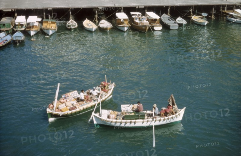 Bumboats at Port Said'. Two bumboats filled with trade wares float in the harbour at Port Said. Several smaller boats are moored to a jetty nearby. Port Said, Egypt, 1958. Port Said, Port Said, Egypt, Northern Africa, Africa.