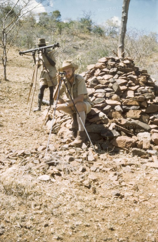 Surveying with 'kituti' markers. District Forest Officer James Lang Brown (right) is accompanied by Forest Ranger Langoya on a survey safari in the Karasuk hills on the Kenya-Uganda border. The men use a range finder and compass to measure the distance between one 'kituti' (cairn) marker and the next. A related caption comments: "When plotted on the map, the line of bituti... will form the legal boundary of a new forest reserve from which marauding goats will be excluded". Kenya, 1959., East (Uganda), Uganda, Eastern Africa, Africa.