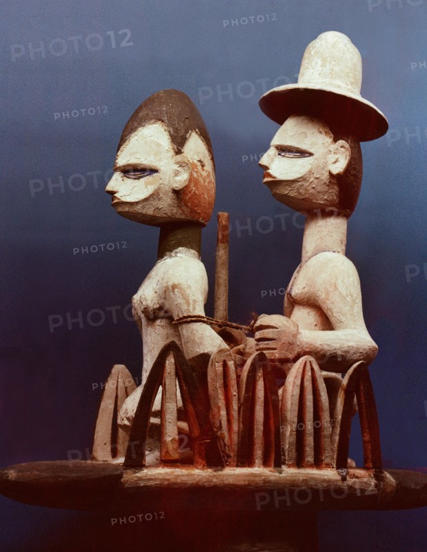Wooden dance headdress showing a slave trader, wearing a European hat, with his woman captive