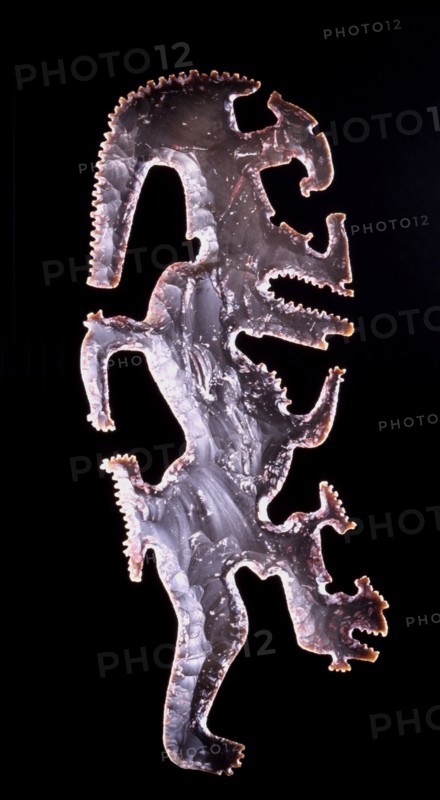 Eccentric axe with representation of the God K, the god of lightning, recognised by the torch running through his forehead and an elongageted serpentine leg