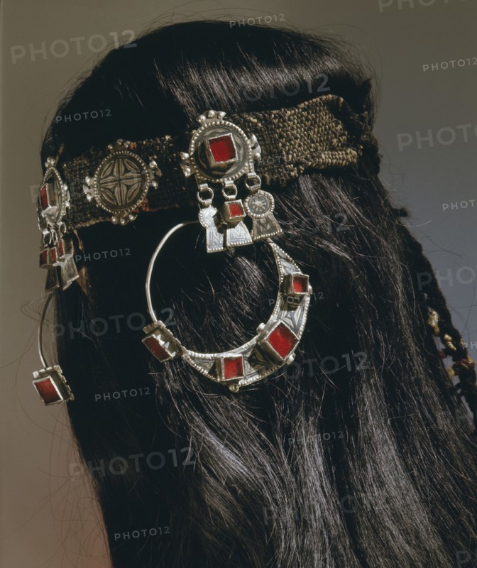 A silver headband from which hang large circular earrings inlaid with glass