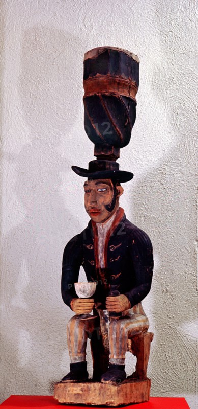 Drum with support carved as the figure of a seated European trader with gin bottle and glass