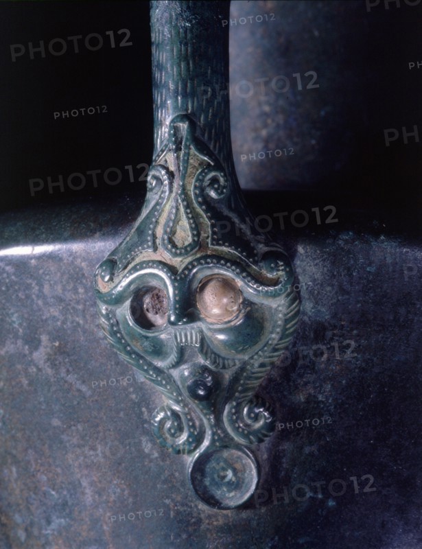 Lower handle attachment of a bronze jug represents a bearded and moustached head which is crowned with an emblematic representation of the Tree of Life