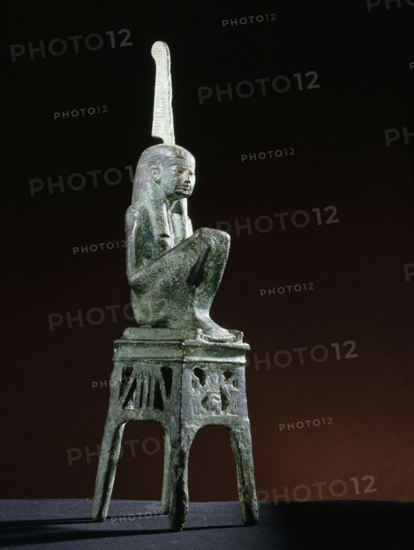 Seated bronze figure of the goddess Maat, wearing a tripartite wig, seated on an openwork throne of winged uraei and Hathor heads